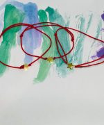 Brățară copii cu șnur roșu și stea aurie pe fundal colorat pictat manual